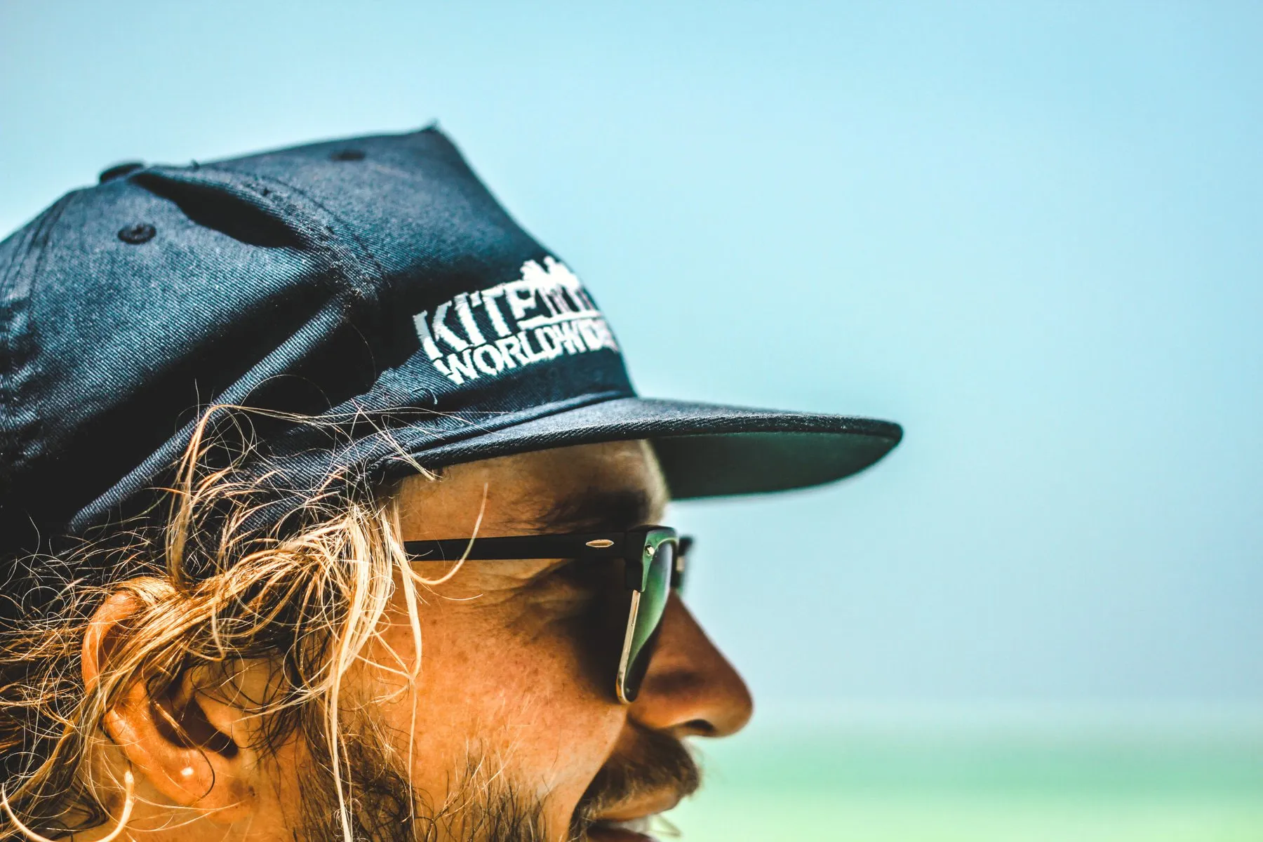 Profil-Porträt eines Mannes mit Kite-Cap und Sonnenbrille am Strand